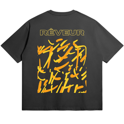 Oversized black streetwear t-shirt “LUCID SPARKS” by RÊVEUR — bold abstract orange and yellow brushstroke design symbolizing creative energy and artistic freedom.