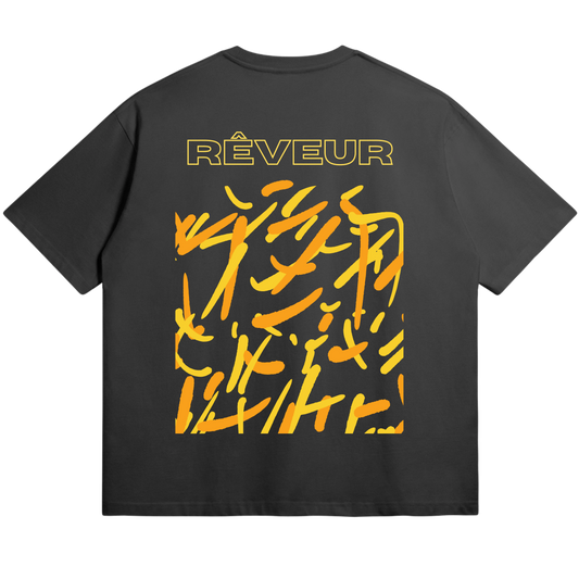 Oversized black streetwear t-shirt “LUCID SPARKS” by RÊVEUR — bold abstract orange and yellow brushstroke design symbolizing creative energy and artistic freedom.